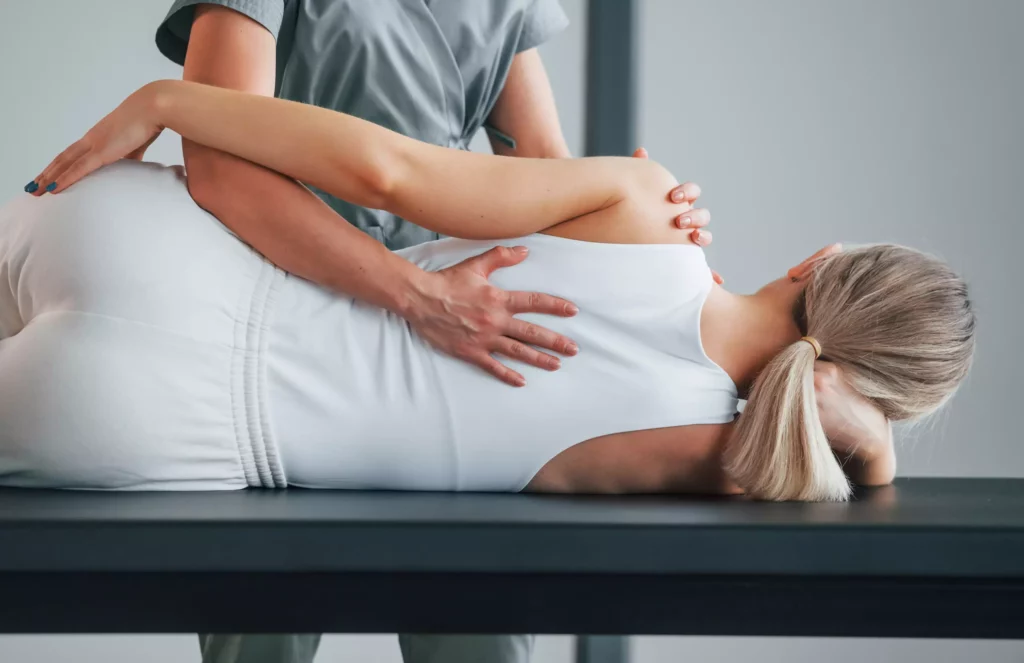 Therapeutin führt manuelle Therapie an liegender Frau auf Behandlungsliege in hellem Raum durch