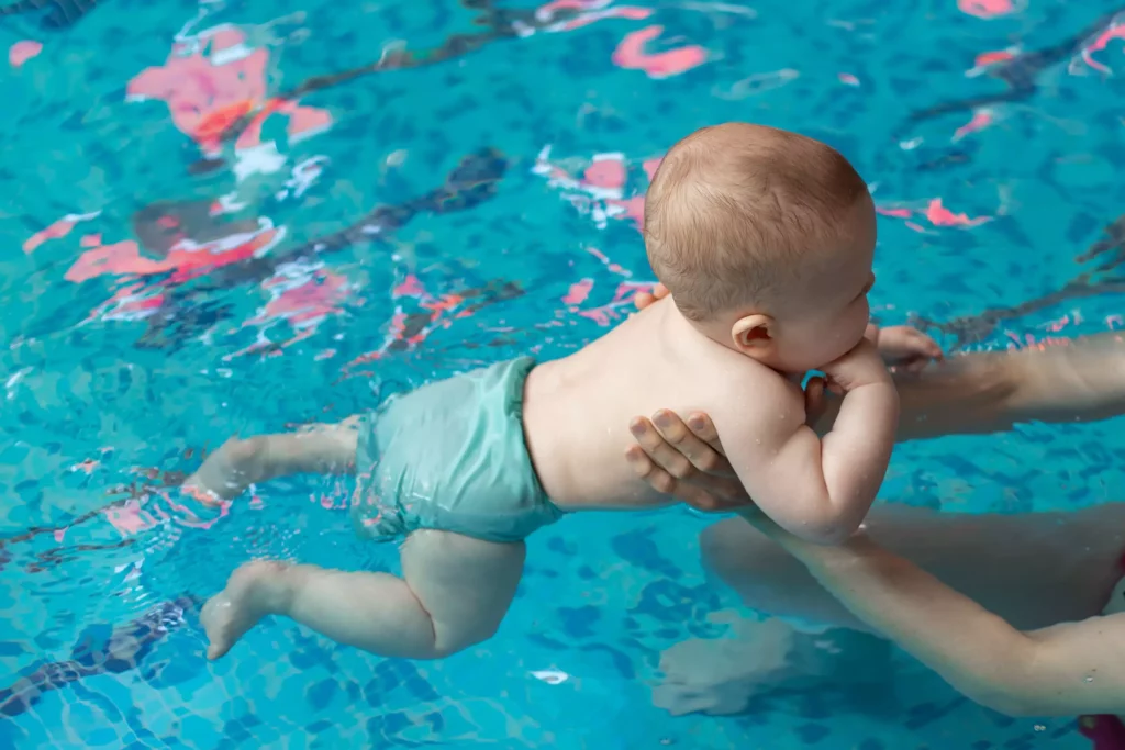 Baby mit Schwimmwindel wird von Erwachsenen im Schwimmbecken gehalten und lernt schwimmen