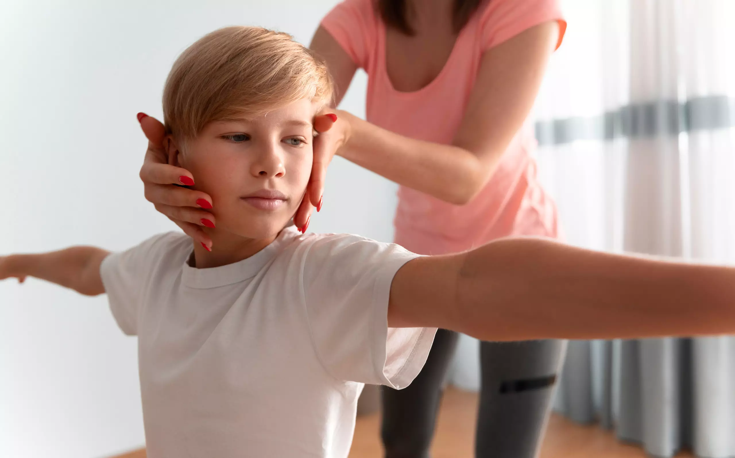 Kind mit ausgestreckten Armen erhält sanfte Therapieunterstützung von Erwachsener im hellen Raum
