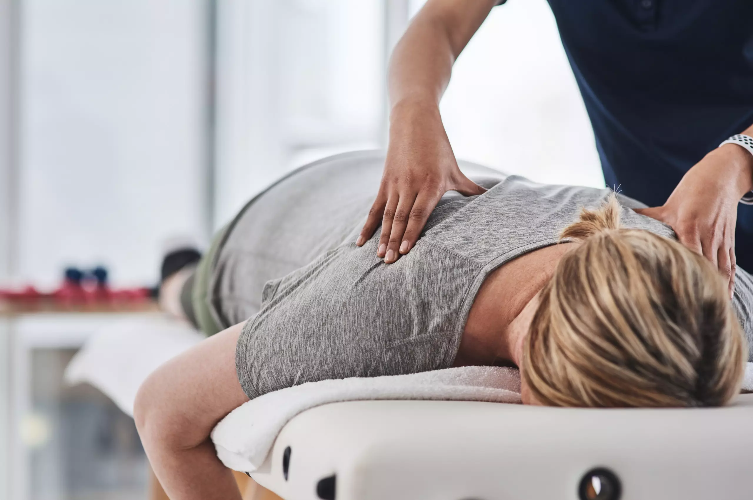 Frau liegt auf Massageliege und erhält Rückenmassage von Therapeut in heller Praxis für Therapiezentrum